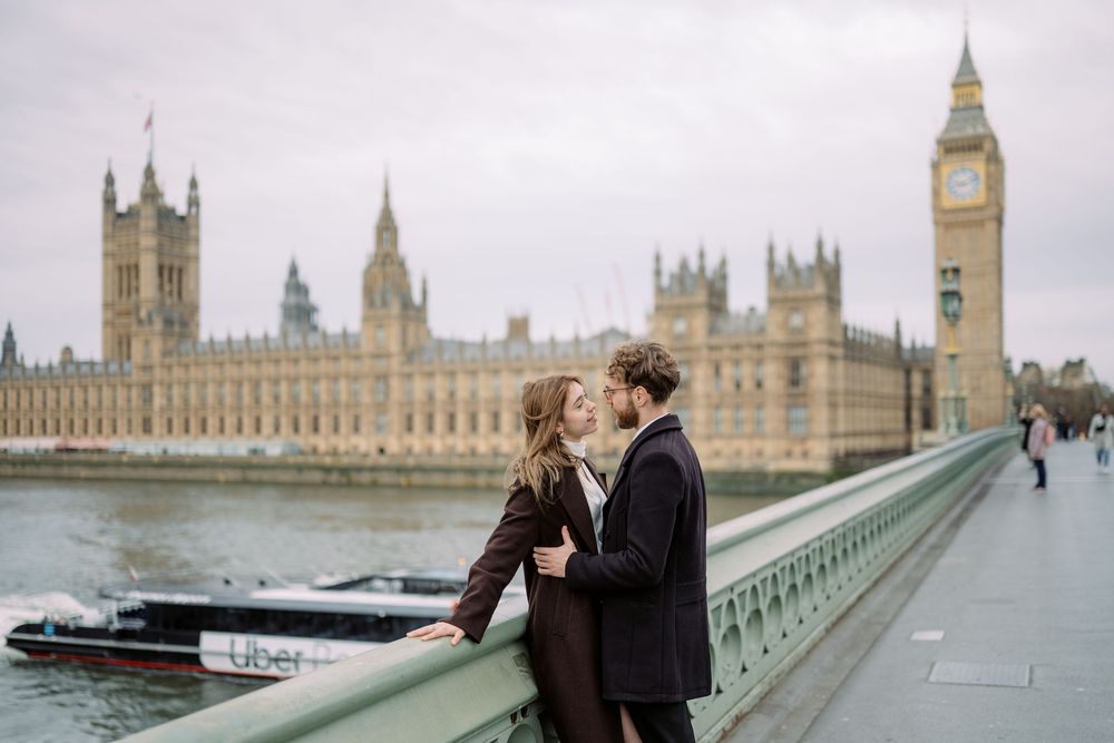 A romantic couple embraces on Westminster Bridge with the iconic Houses of Parliament and Big Ben in London as backdrop.