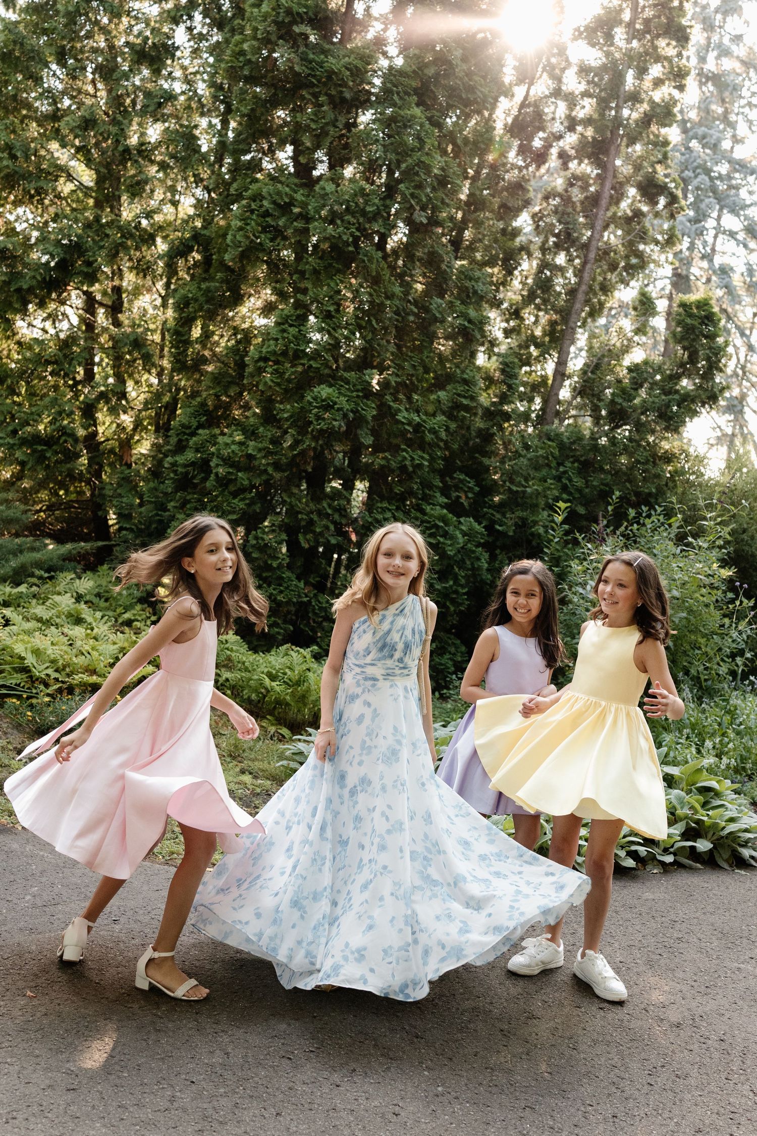 Four girls in pastel dresses twirl and dance outside. Candid Montreal Wedding Photography by Aliza Dworkind. Captured on 35mm film.