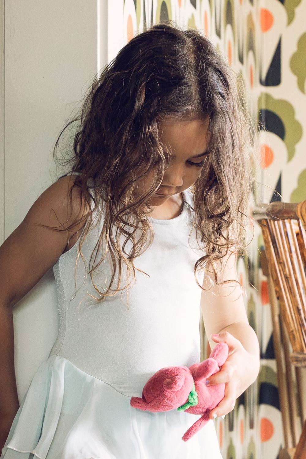 A young girl in a white ballet dress examines a pink stuffed bunny toy.