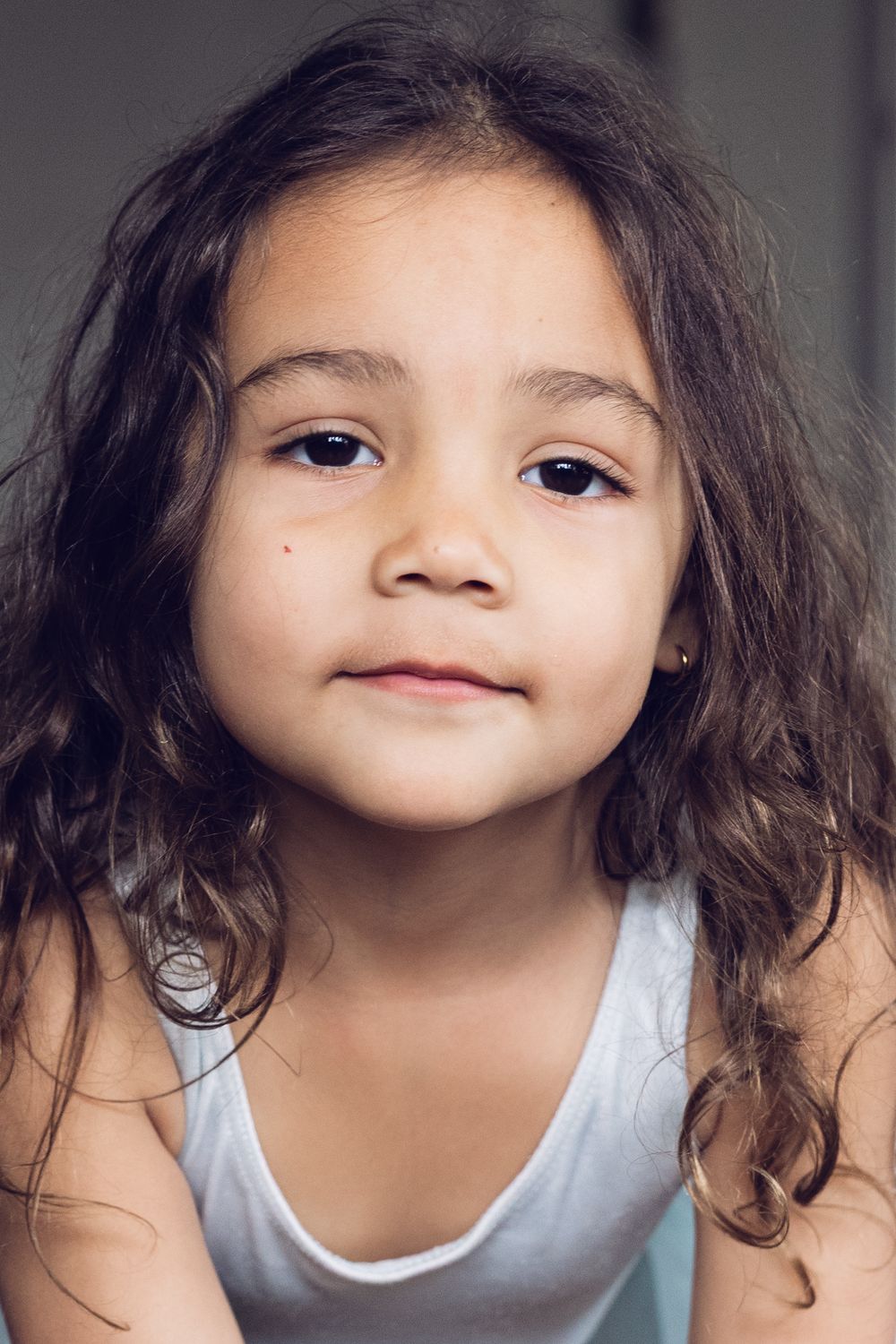 A close-up portrait of a young girl with curly dark hair and a gentle smile.