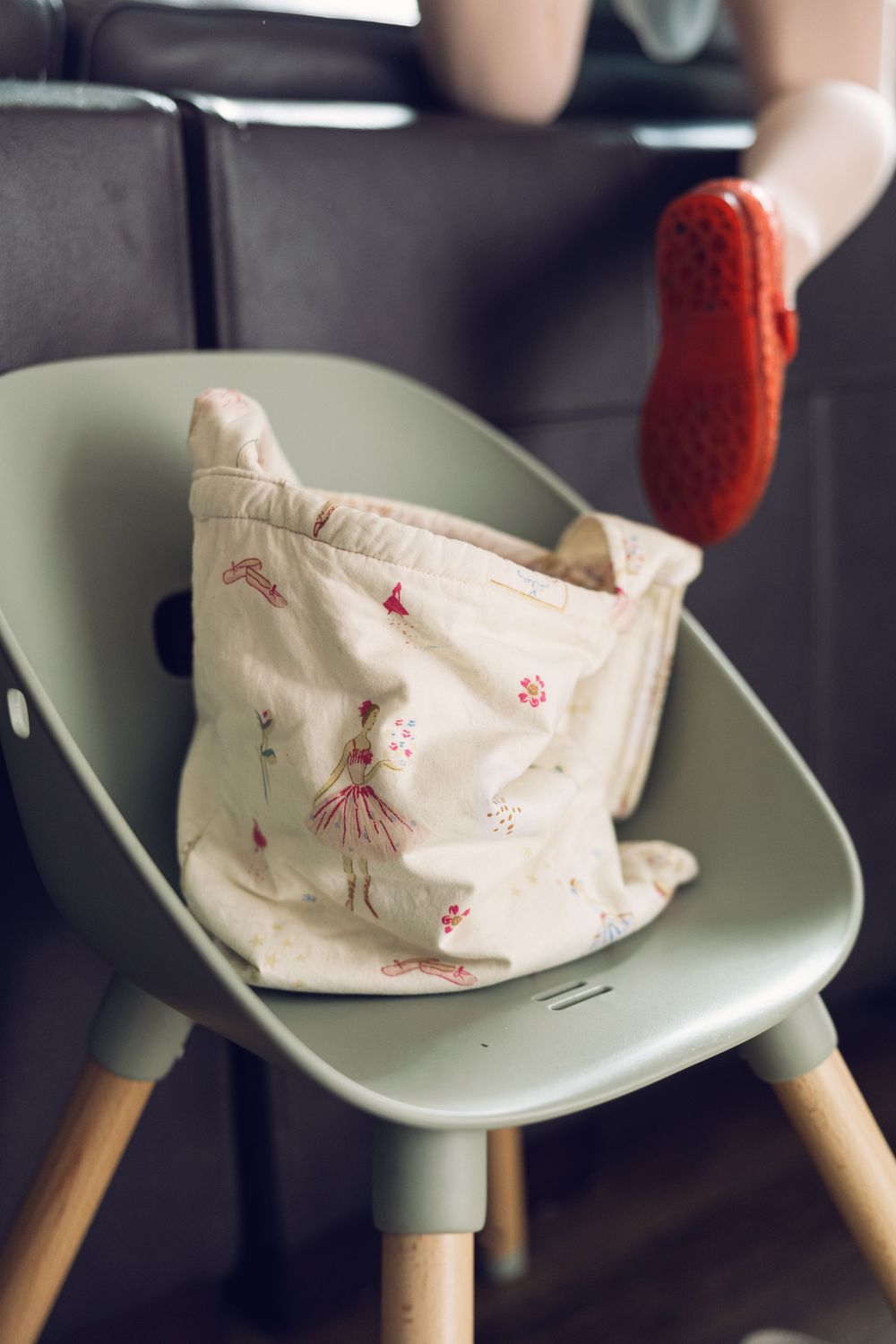 A decorative fabric bag with ballerina print rests on a modern green children's chair.