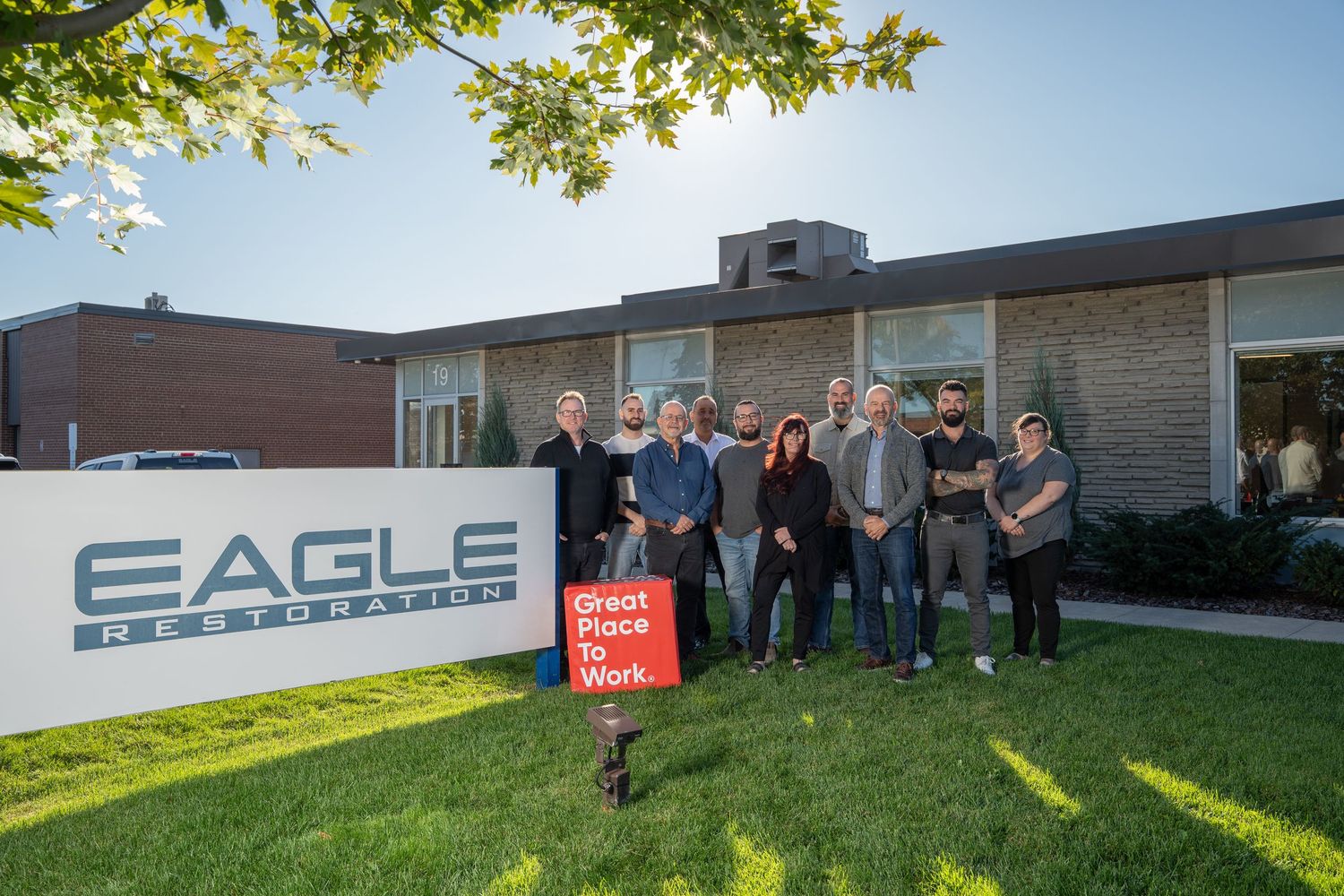 A group of people standing outside an Eagle Technology building with a company sign and green lawn.