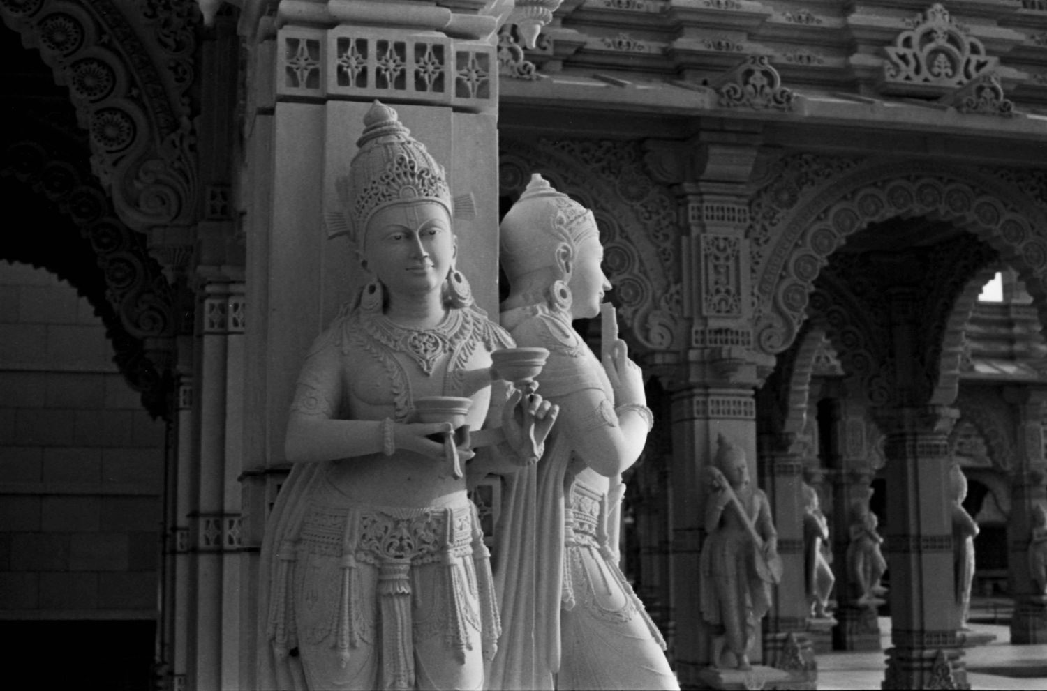Ornate carved stone statues stand in an elaborate temple corridor with arched architectural details.