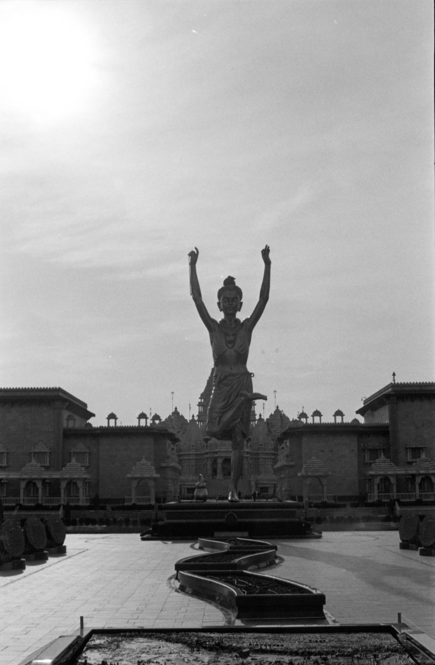 Silhouetted figure stands triumphantly on a rooftop with arms raised against a cloudy sky in black and white.