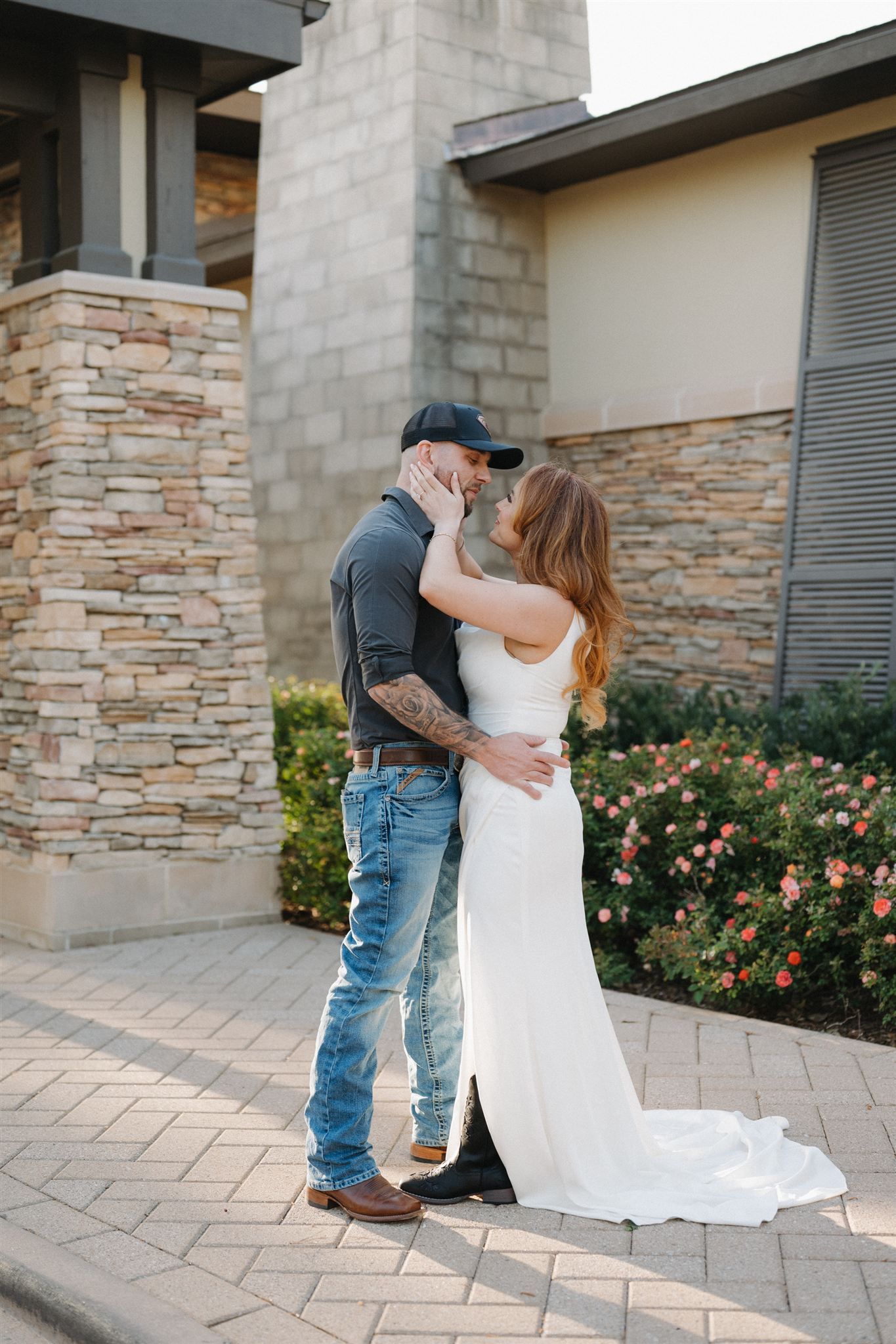 A couple in wedding attire embraces on a stone paver patio outside The Woodlands Resort, a modern building with stacked stone walls.