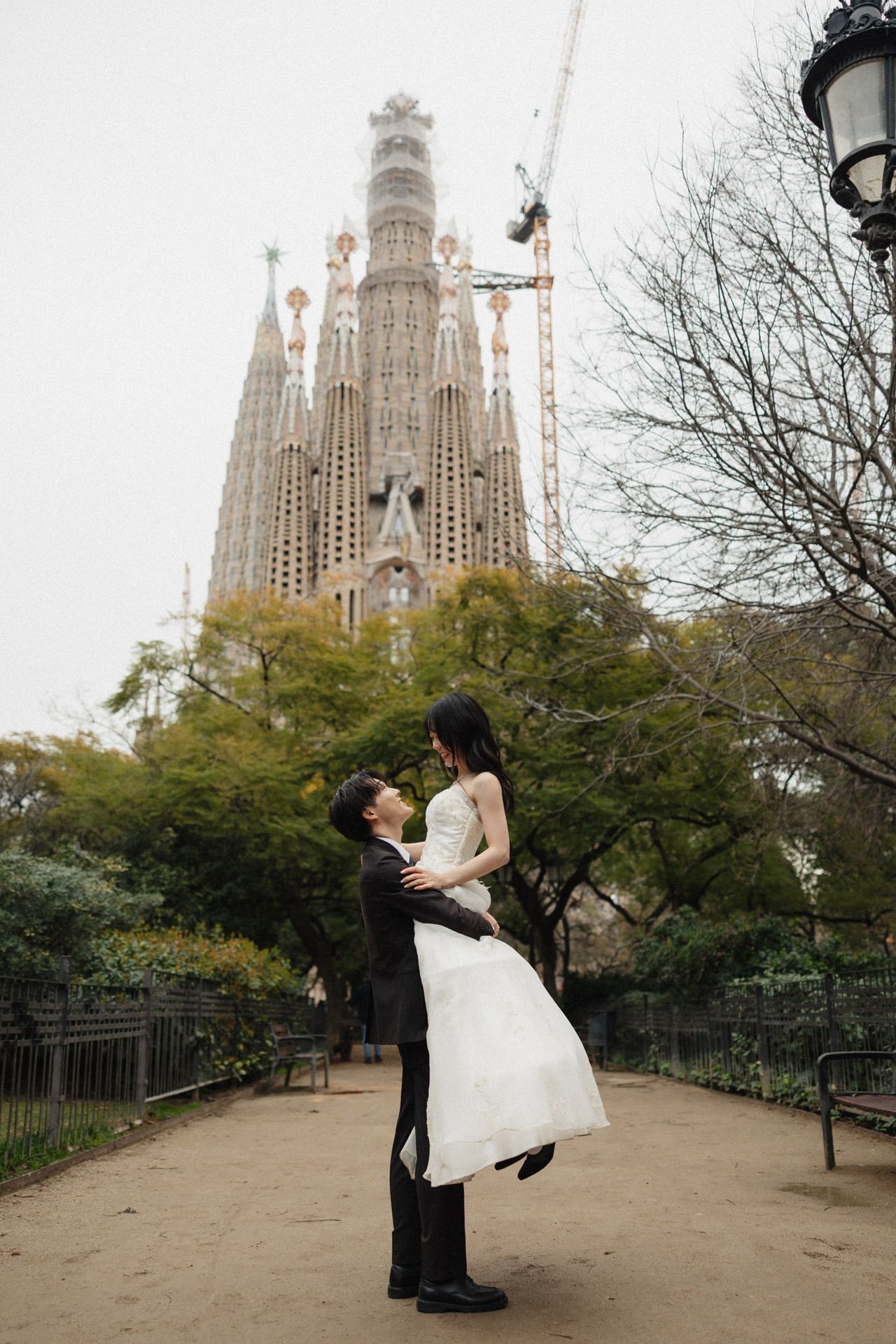 A romantic couple poses in front of the iconic Sagrada Familia cathedral in Barcelona during golden hour.