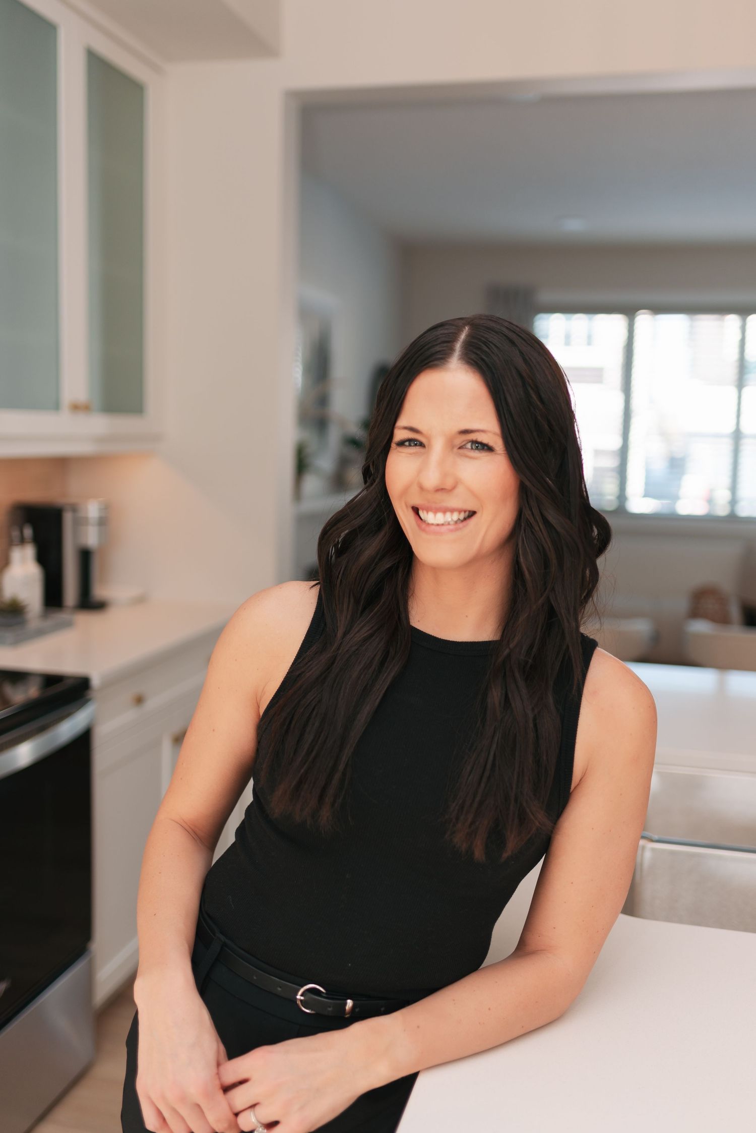 Professional headshot series of a person in a black sleeveless top smiling against a bright modern interior background.