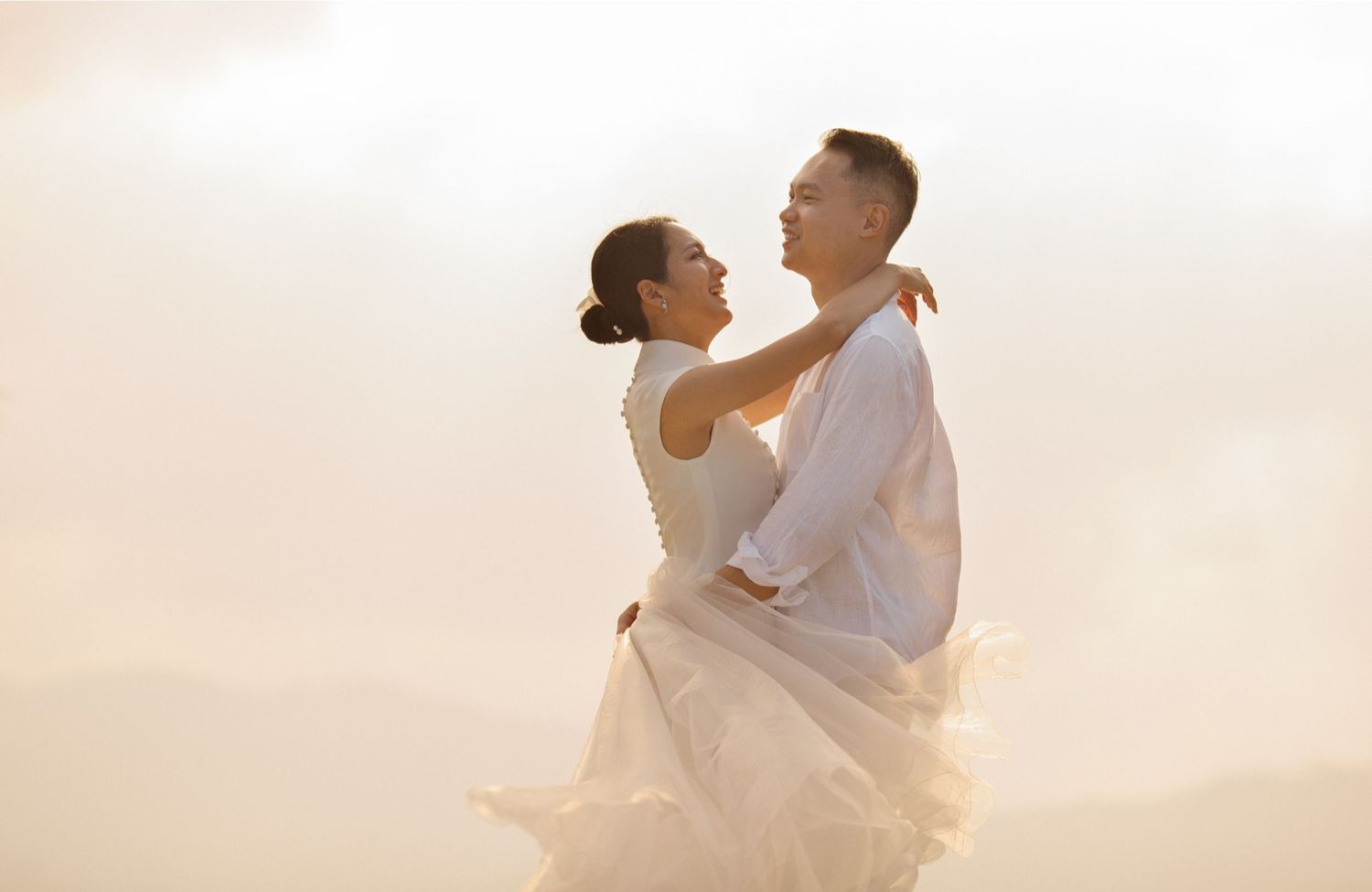 Bride in an elegant white cheongsam smiles as she embraces her groom at a romantic Koh Samui beach wedding