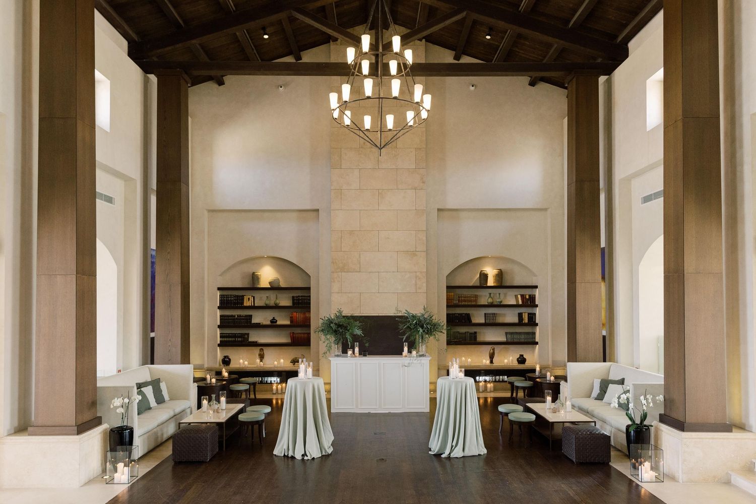 Elegant wedding venue interior with exposed wooden beams, chandeliers, and white drapes in a panoramic view.
