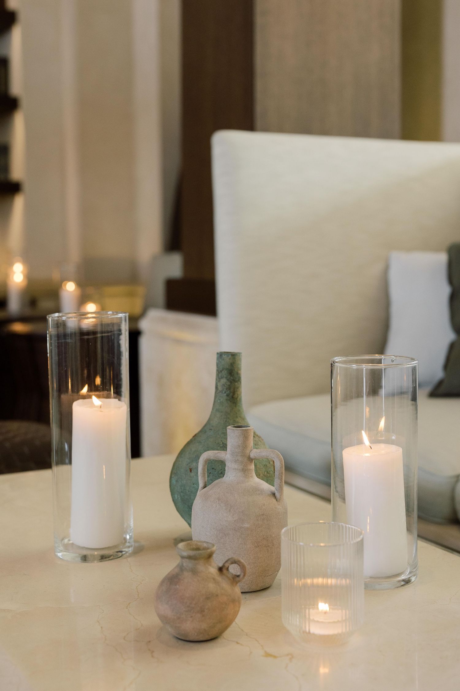 Lit white pillar candles in glass holders alongside vintage ceramic vases create an elegant centerpiece display.
