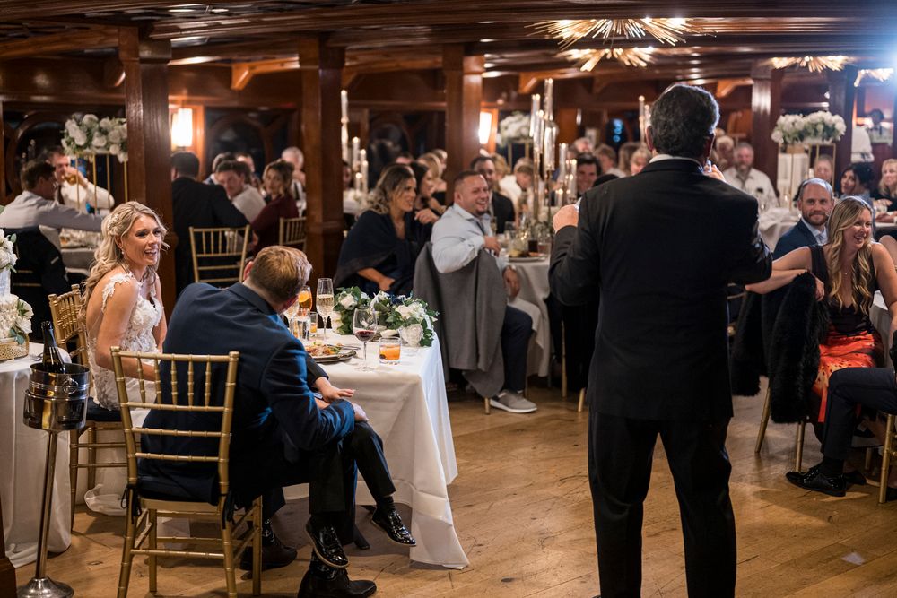 Wedding guests dancing and celebrating on a rustic wooden dance floor at an indoor reception venue.