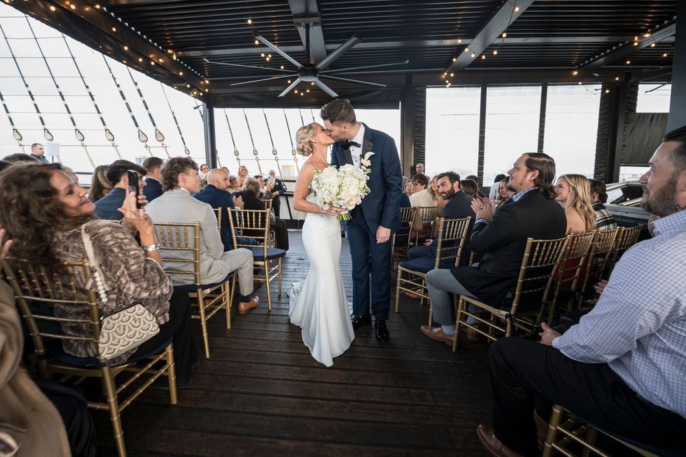 A wedding reception setup in a rustic venue with string lights overhead and wooden chairs arranged at round tables.