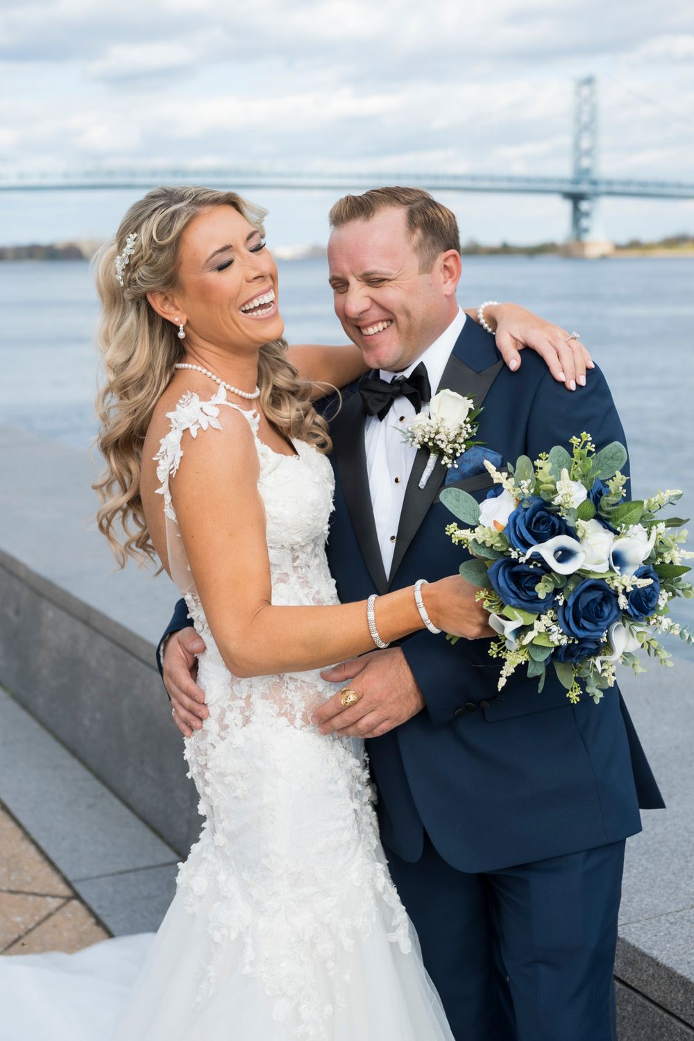 A joyful couple shares a candid moment together on their wedding day with the Ben Franklin Bridge in the background.