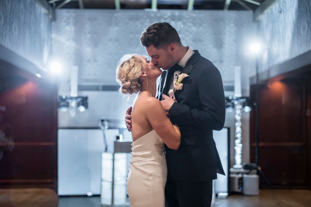 A couple shares their first dance at their wedding reception in a dimly lit ballroom with dramatic lighting.