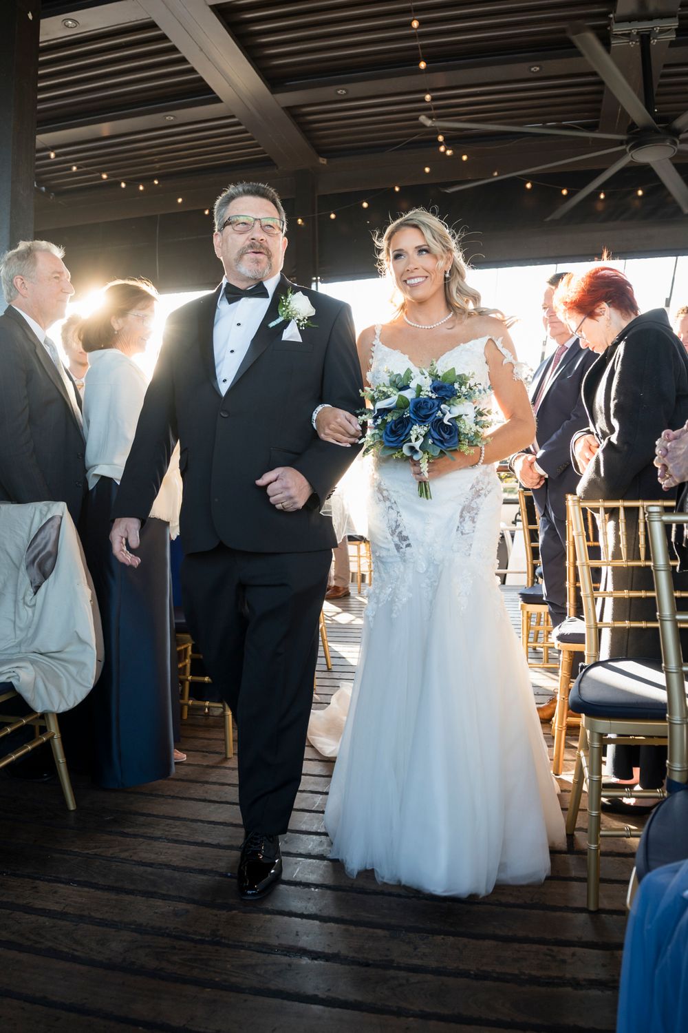 Wedding party mingles and socializes during reception in rustic venue with wooden floors and twinkling lights.