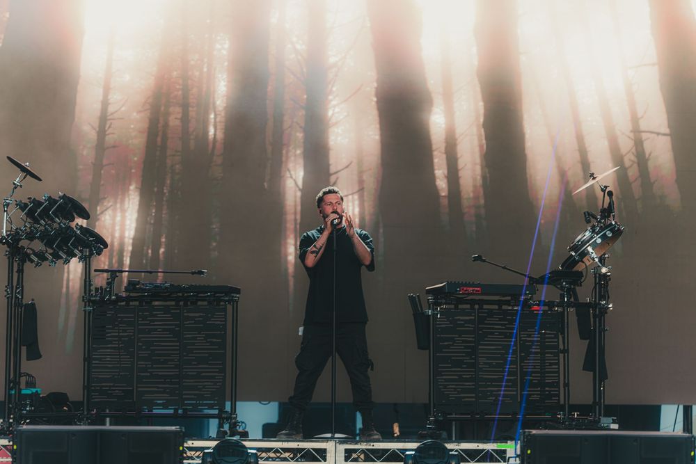 Silhouetted performers on stage with pink and white backlit curtains creating a dramatic concert atmosphere.