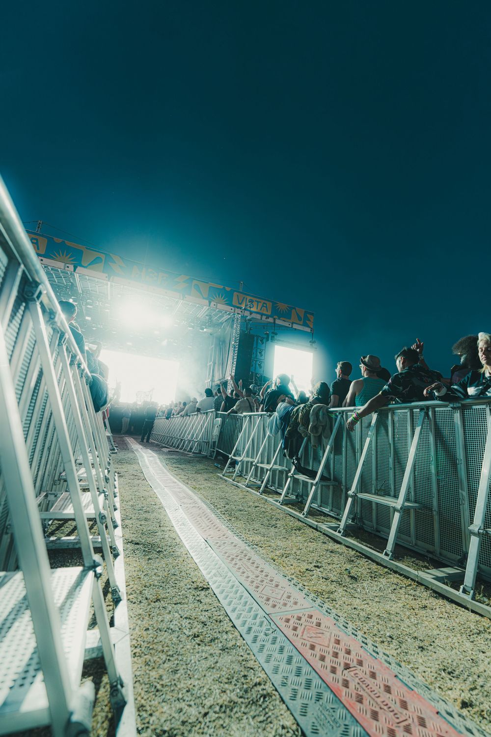 A nighttime view of illuminated barriers and walkway with crowd silhouettes creating an atmospheric scene.