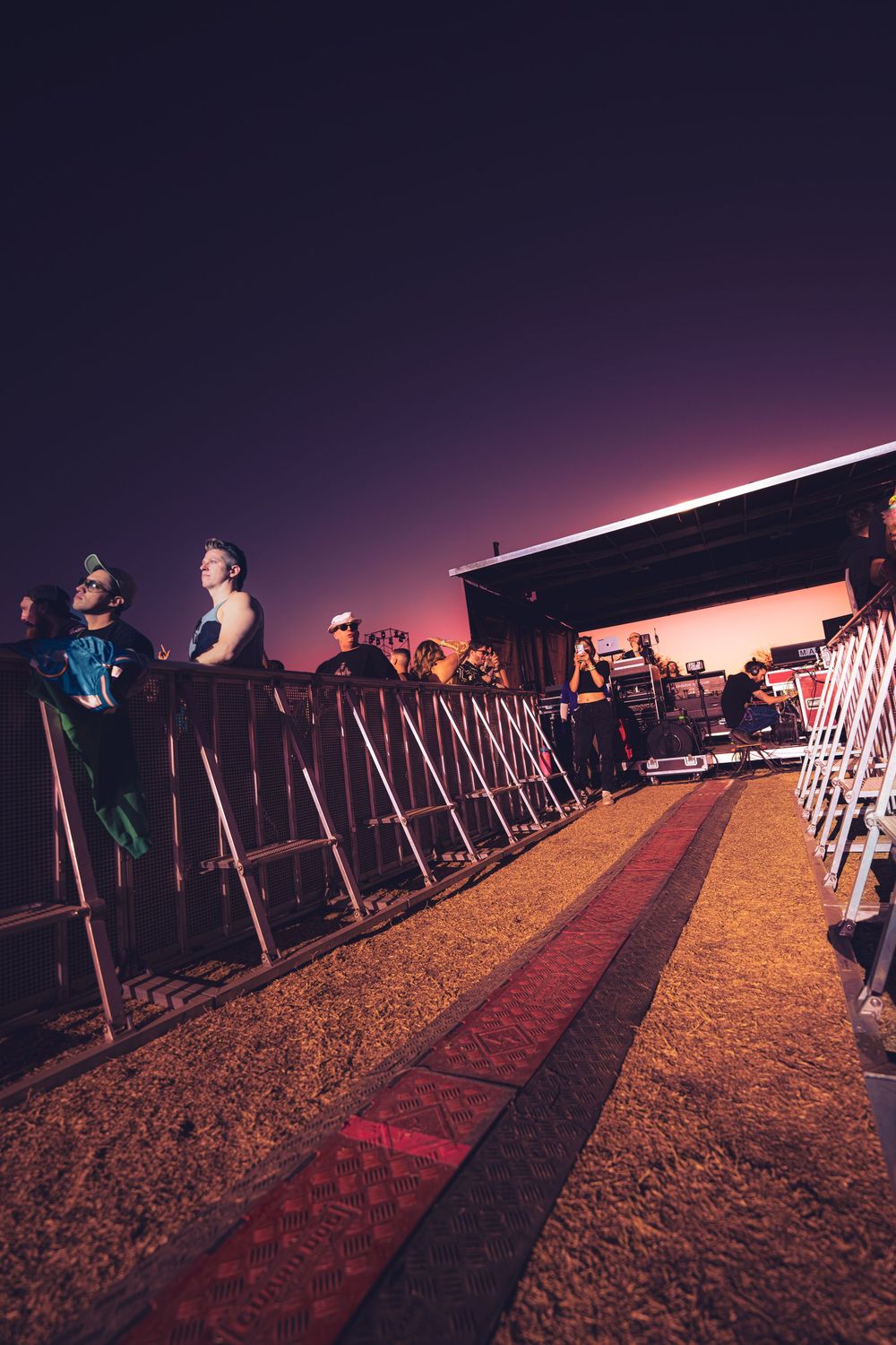 People seated in rows of chairs at an outdoor event during sunset, casting long shadows across the ground.