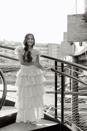A white ruffled dress captured in black and white against an urban balcony setting.
