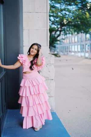 A pink tiered ruffle dress photographed against concrete columns in an urban setting.