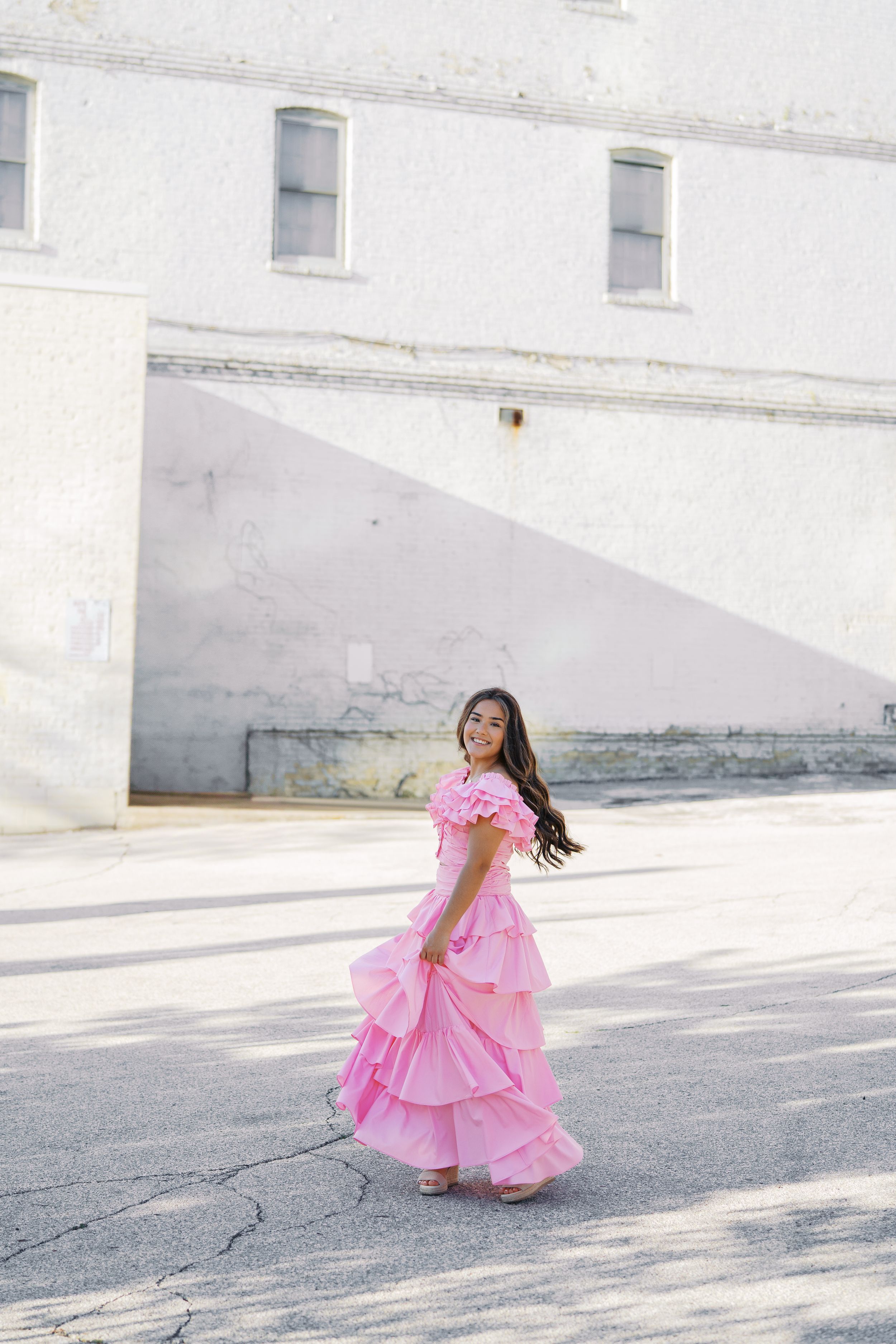 A flowing pink dress captured in motion against a white urban backdrop.