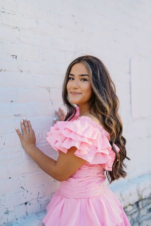A pink ruffled dress photographed against a white brick wall in natural lighting.