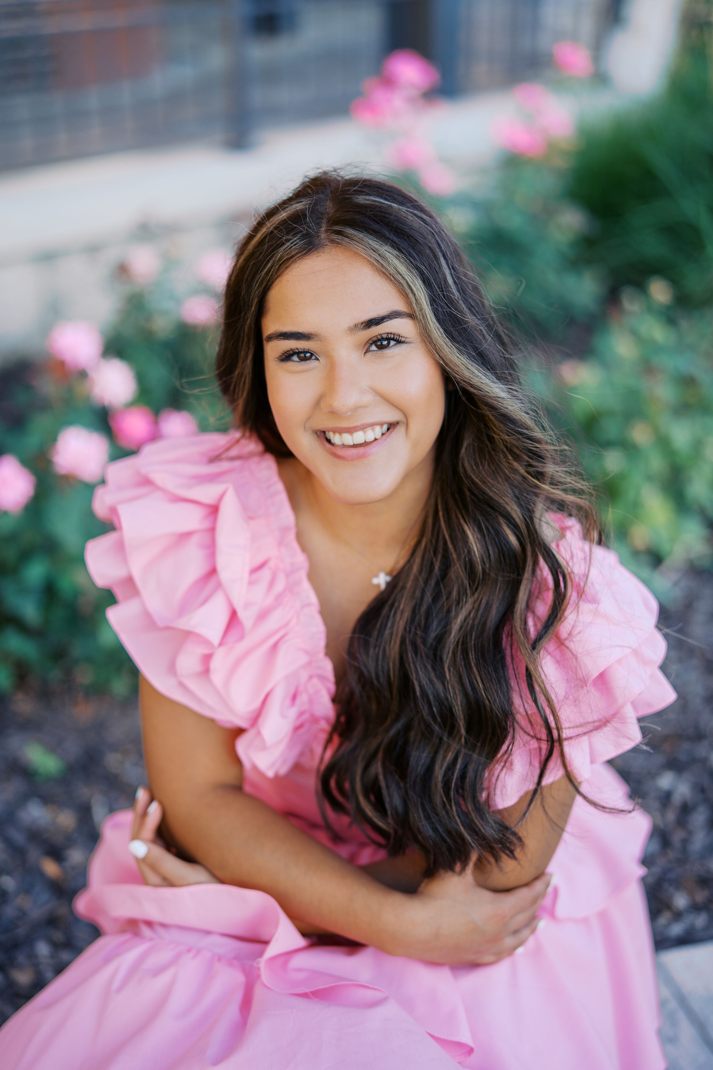 Portrait in a pink ruffled dress against a garden backdrop with blooming pink flowers.