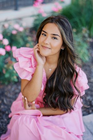 Outdoor portrait with pink ruffled dress and floral garden setting.