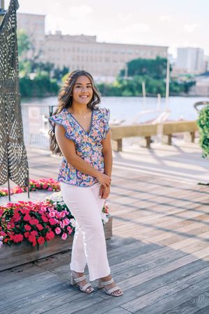 Standing on a waterfront deck wearing white pants and a floral top with ruffled sleeves.