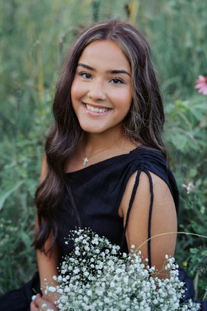 Outdoor portrait in black dress holding baby's breath flowers against natural greenery.