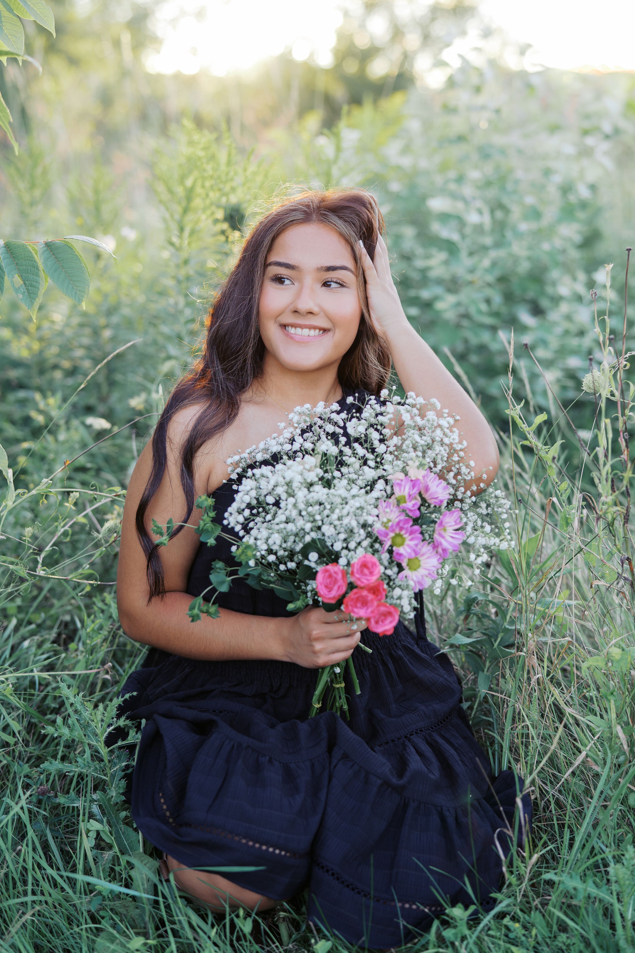 Summer portrait in navy dress holding mixed bouquet of pink and white flowers in tall grass.