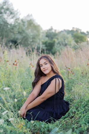Artistic portrait session in tall grass and wildflowers with soft natural lighting and black dress.