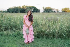 Whimsical outdoor photography in a flowering meadow with pink ruffled dress.