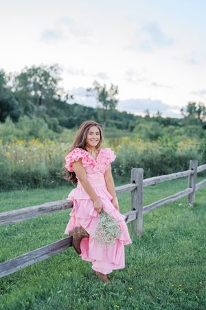 Country rustic photoshoot by wooden fence featuring pink ruffle dress and wildflowers.