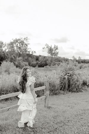 Artistic black and white portraits in flowing white dress by rustic fence.
