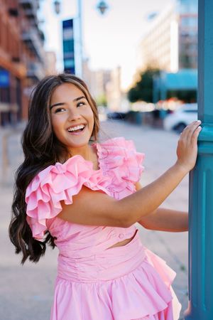 A pink ruffled dress creates a striking contrast against an urban cityscape background.