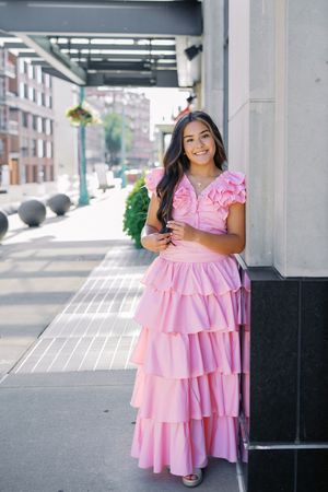 A pink ruffled dress photographed against an urban backdrop with columns and outdoor seating.