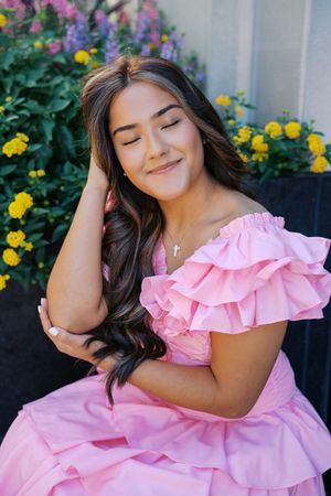 A pink ruffle dress shown against a backdrop of colorful flowers and greenery.