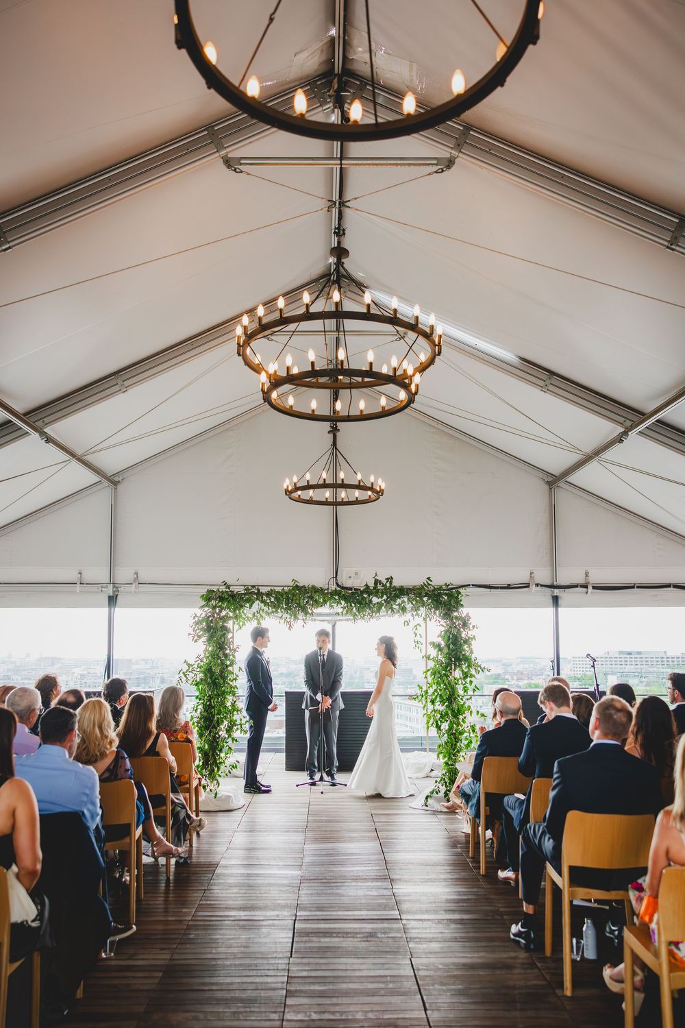 A panoramic view of the line DC ceremony space under a white tent with rustic chandeliers and greenery decor.