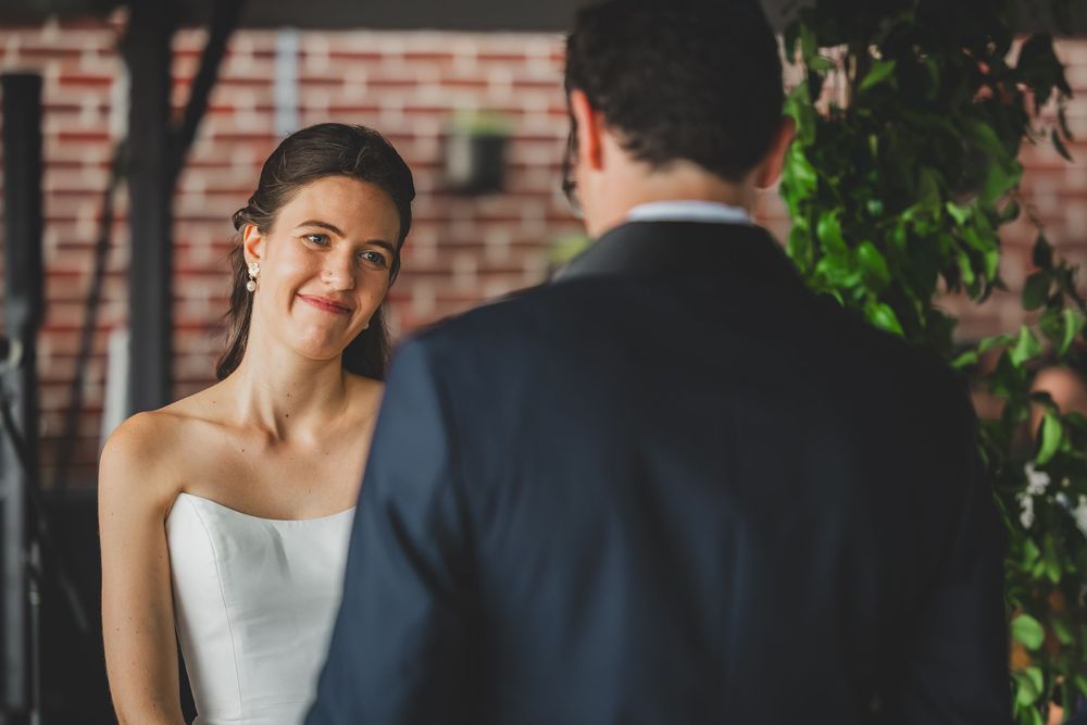 A couple shares a romantic moment during their wedding ceremony against a brick wall backdrop.