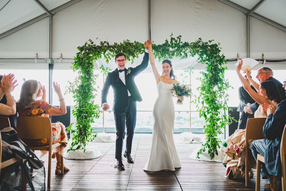 A joyful celebration under a lush green floral arch as newlyweds celebrate with guests at an outdoor wedding ceremony.