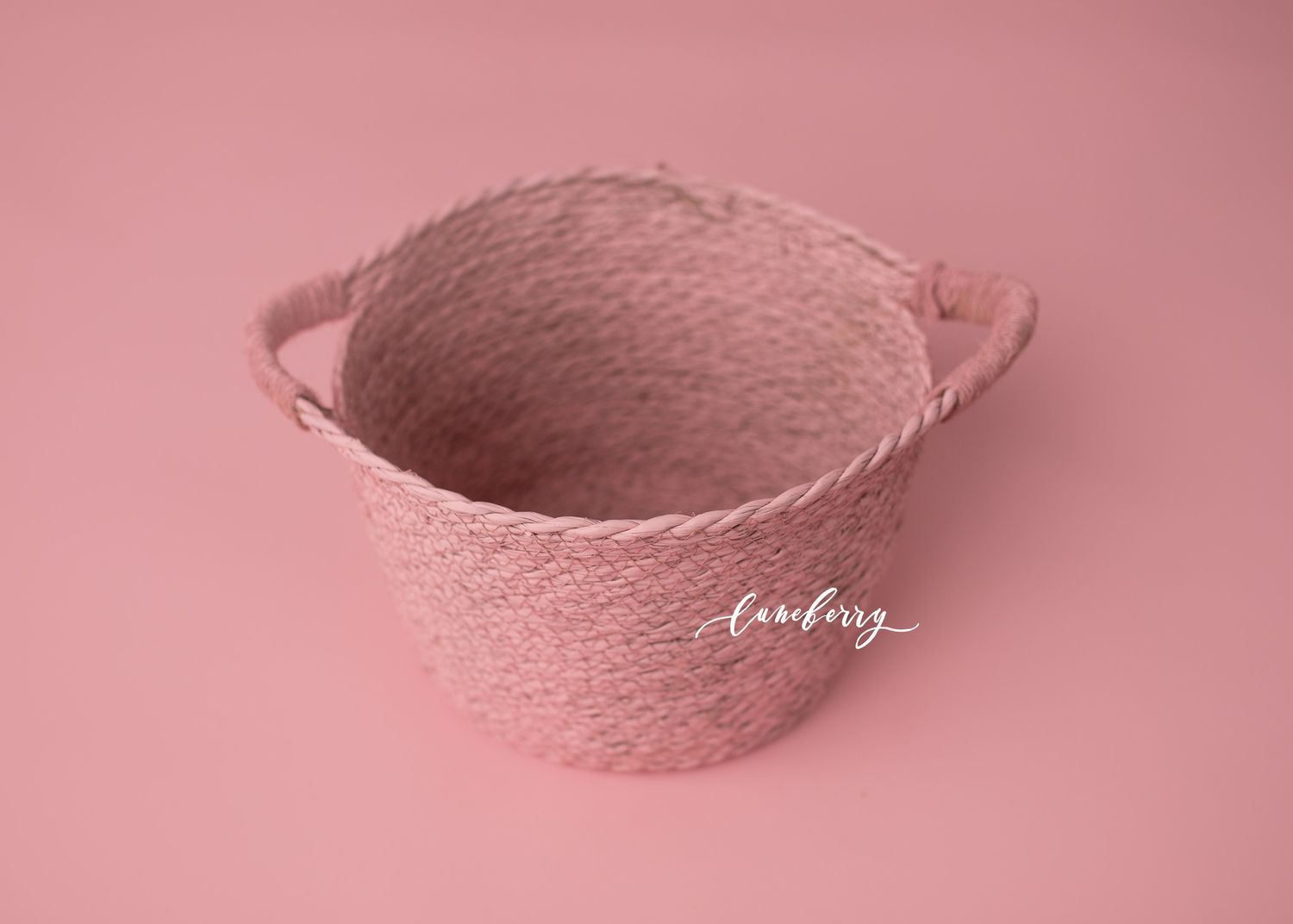 Pink woven rope basket with handles on a pink background, ideal for newborn photography props.