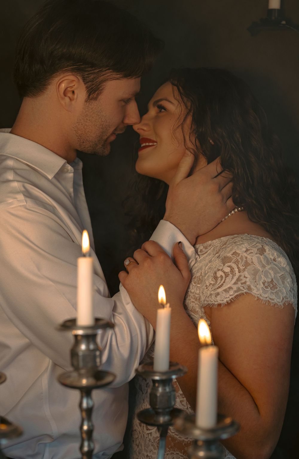 A romantic candlelit scene with a couple in wedding attire embracing in soft lighting.