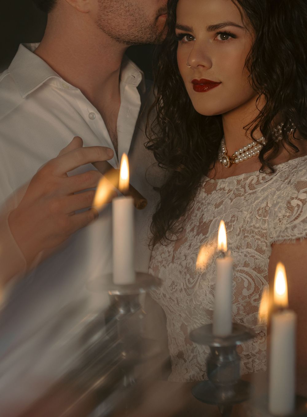 Intimate portrait with candlelight featuring white lace dress and pearl necklace details.