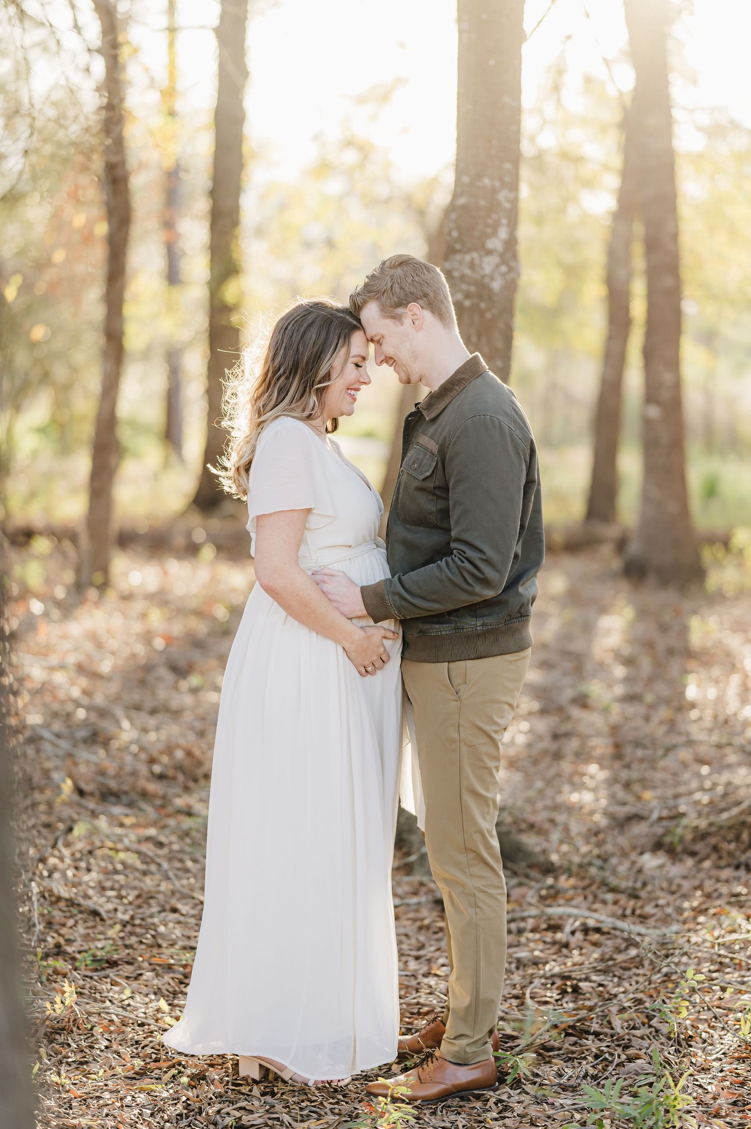 Romantic couple shares a tender moment in a sunlit autumn forest while wearing white and khaki casual attire houston maternity photographer