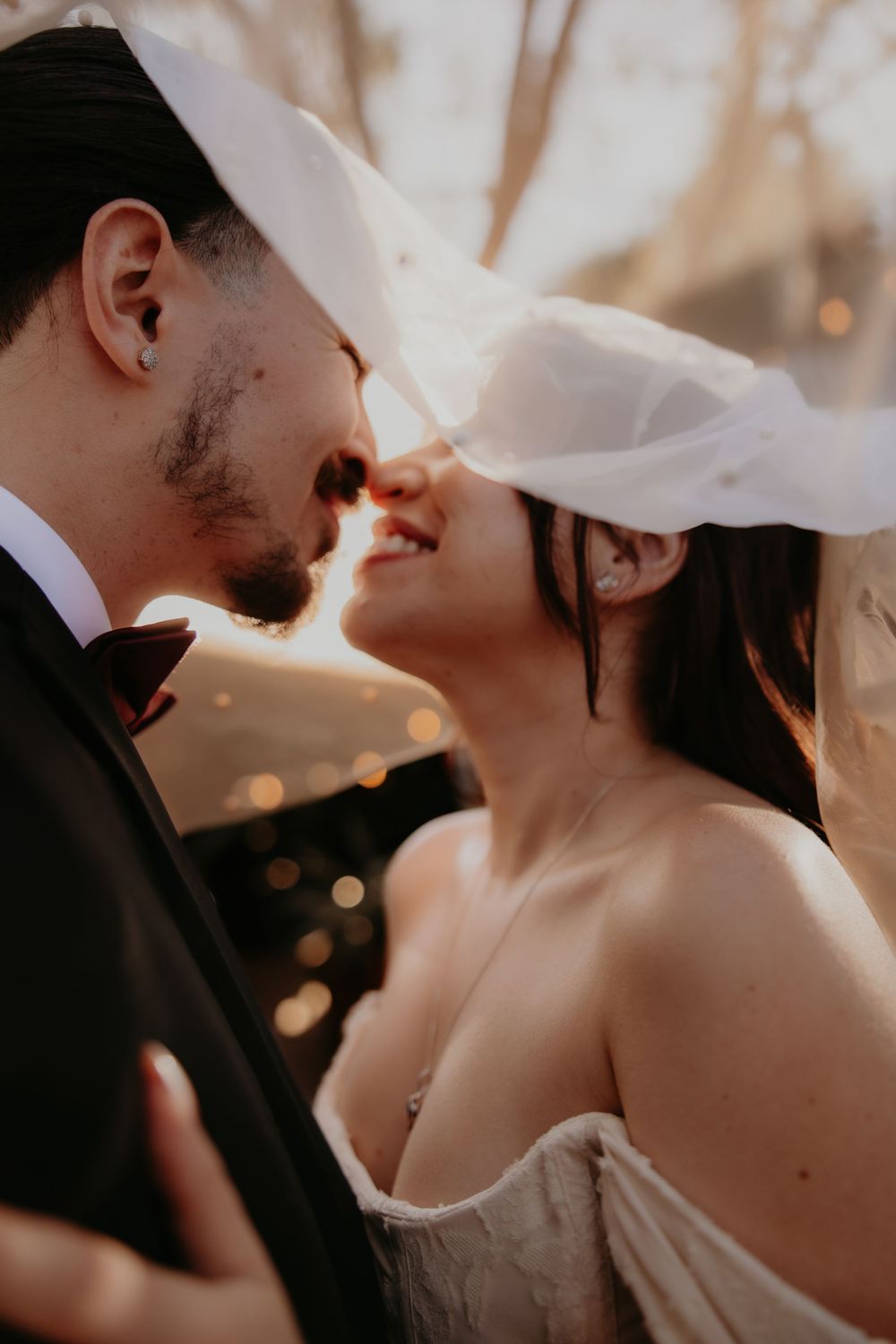 A bride and groom share a romantic moment under a flowing veil, bathed in warm golden light at their wedding.