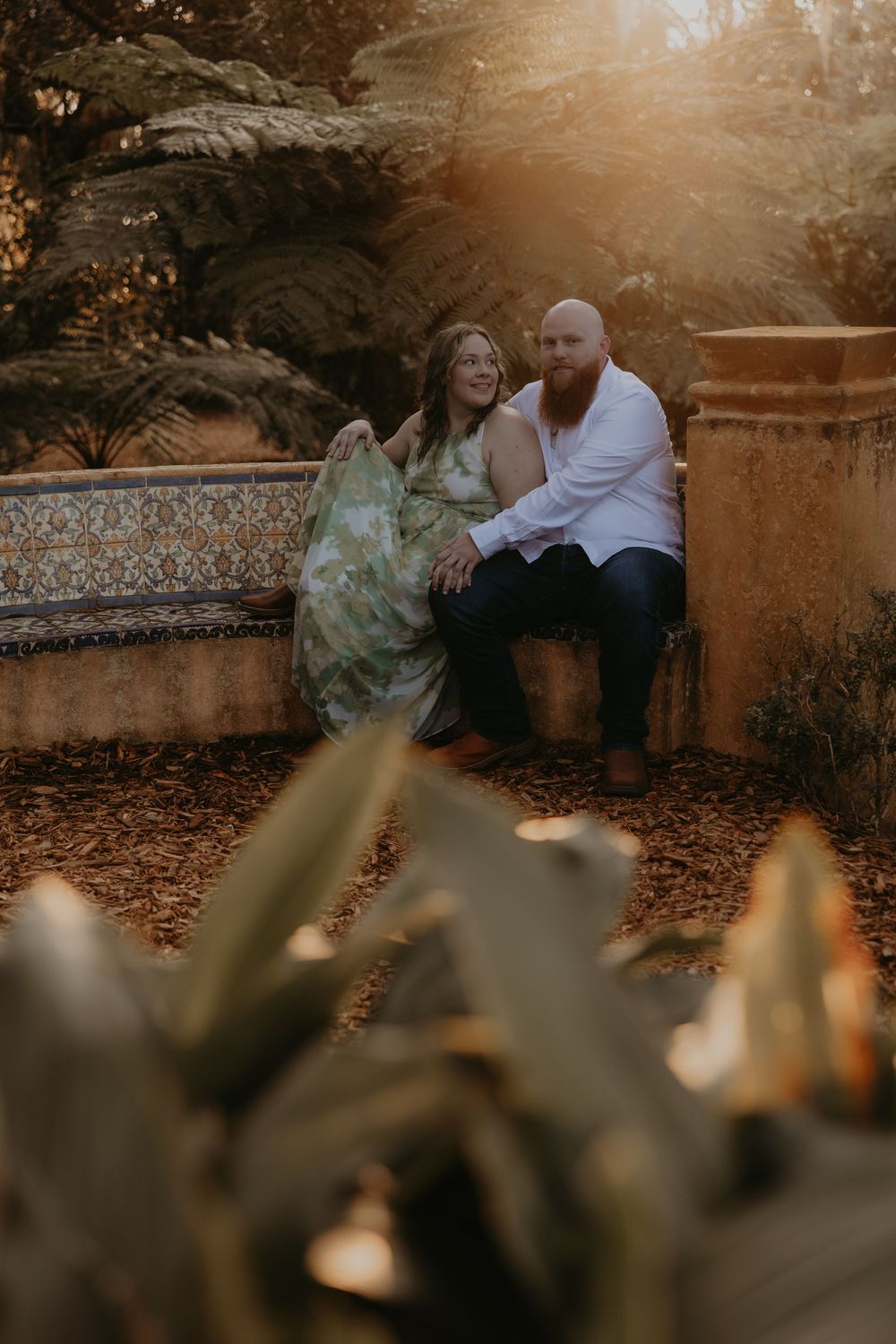 Romantic couple sitting together on stone steps surrounded by autumn leaves during golden hour sunset.