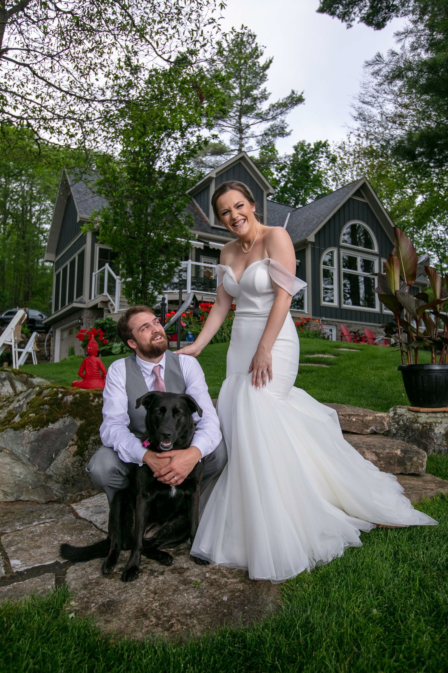 A couple in wedding attire embrace by a tree trunk near a serene lake on their special day.
