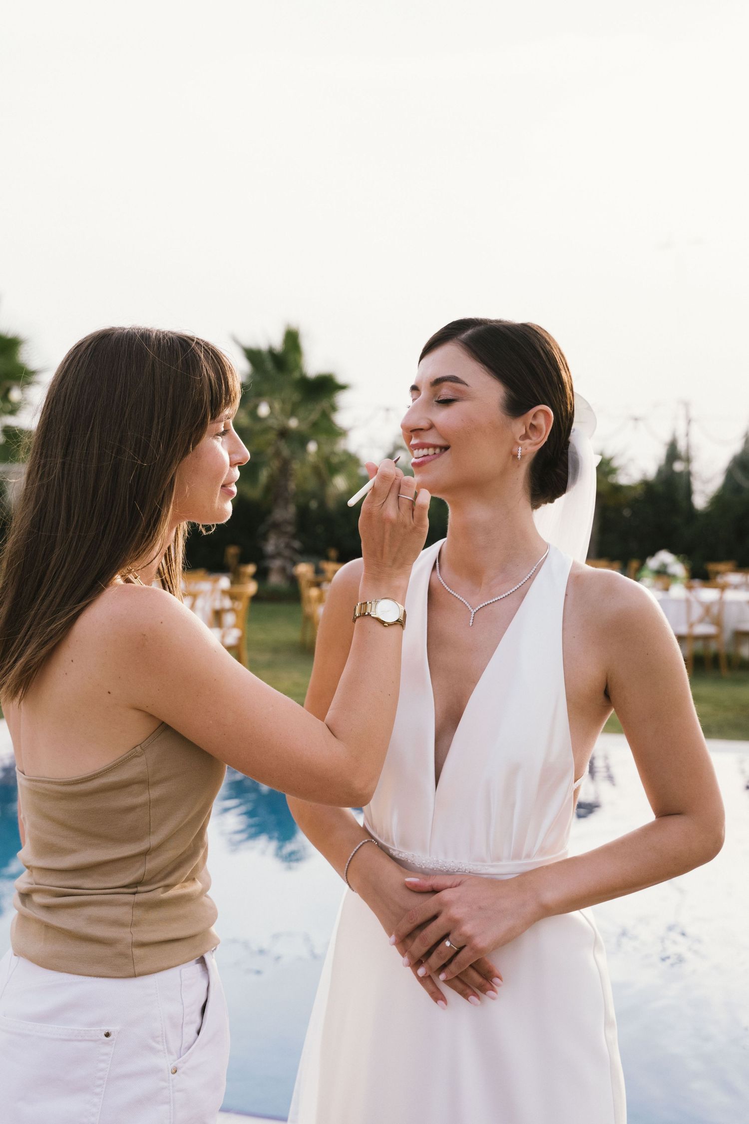 Two people in coordinating outfits share playful moments and laughter by a pool during a summer photoshoot.