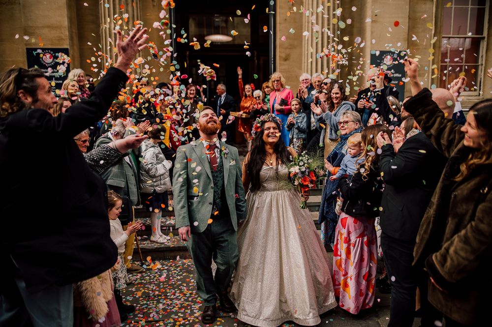 A happy couple celebrates at their wedding ceremony as guests shower them with colorful confetti in a joyous moment.